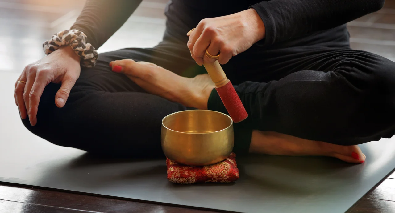 Woman seated cross-legged, focused on a sound bath bowl on a yoga mat.